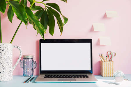 Stylish and creative desk with laptop mock up screen, tropical leaf, office accessories and memo...