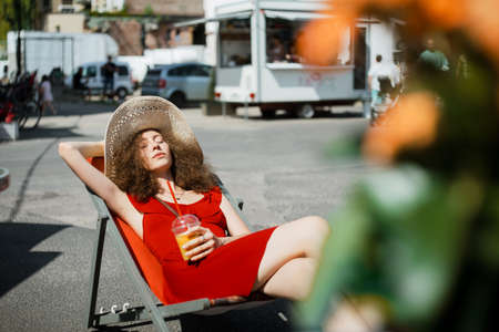 Summer portrait of young beautiful woman on the sunbed . Wearing cute red trendy dress, drinking tasty smoothie, smiling enjoy her weekends, holiday.の写真素材