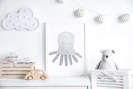 Stylish scandinavian newborn baby shelf with mock up photo frame, box, teddy bear and toys. Modern interior with white walls and wooden accessories.の写真素材