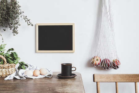 Stylish interior design of kitchen space with small table with mock up frame, herbs, cup of tea, bag with apples and vegetables. Vintage concept of kitchen space..の写真素材