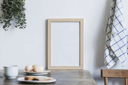 Stylish interior design of kitchen space with small table with mock up frame, herbs, cups of tea and eggs. Minimalistic interior.の写真素材