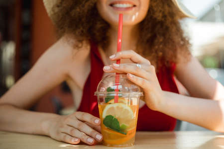 Close up of summer juice with orange and mint in local restaurant. Beautiful woman drinking tasty smoothie, smiling enjoy her weekends, holiday.の写真素材