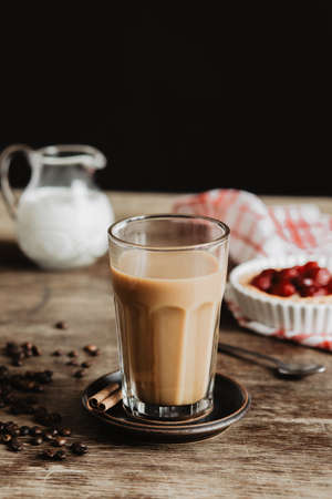 The vintage and stylish composition in kitchen interior with a glass of coffee with milk and cakes. Winter and autumn concept of morning breakfast. Black background.の写真素材