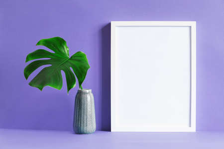 Modern and minimalistic composition of mock up photo frame with green tropical leaf in vase. Stylish concept of mockup frame. Purple background wall.の写真素材