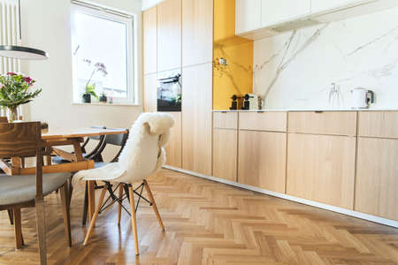 Stylish and cozy scandinavian dining room and kitchen with design family table, chairs and lamp. White and marble walls and brown wooden parquet. Bright and sunny interiorの写真素材