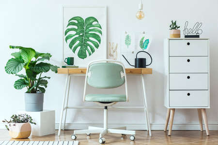 Stylish scandinavian home office desk with mock up poster frames, a lot of plants and office accessories. Brown wooden parquet and white backgrounds wall. Modern composition of homeoffice desk.の写真素材