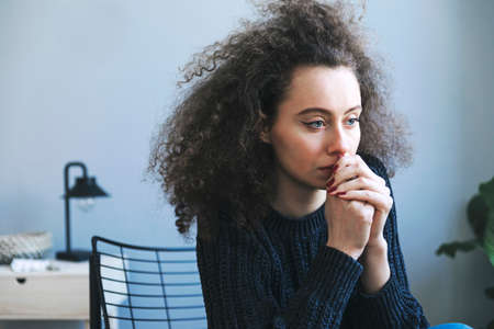 Dark hair teenager with depression sitting alone on the armchair in gray room. Sadness, nostlagic, depression. Mental problems of young people.の写真素材