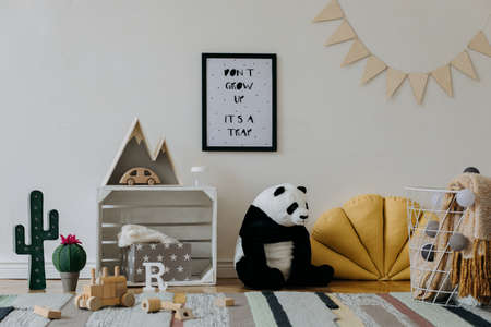 Stylish scandinavian kid room with mock up photo poster frame on the pattern wall, boxes, teddy bear and toys. Cute modern interior of playroom with white walls, wooden accessories and colorful toys.の写真素材