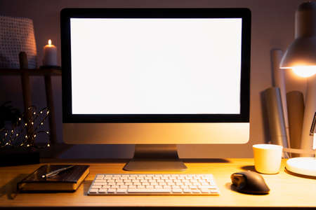 Stylish scandinavian interior of home creative desk by night with mock up computer screen, plants, office accessories and notes. Minimalistic space for work, hobby and listen music. Freelancer space.の写真素材