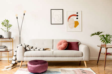 Stylish retro interior of sitting room with design sofa, gold bookstand, vintage table and mock up posters frames on the white walls. Interior design with brown wooden parquet, plants and leafs.の写真素材
