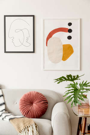 Stylish vintage interior of living room with design sofa, pillow, blanket ,retro table and mock up posters frames on the white walls. Interior design with brown wooden parquet and tropical leafs.の写真素材