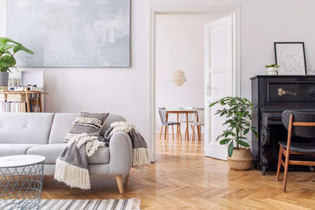 Modern scandianvian decor of living room with design sofa with elegant blanket, coffee table and bookstand on the white wall. Brown wooden parquet. Concept of minimalistic interior with piano. Mock upの写真素材