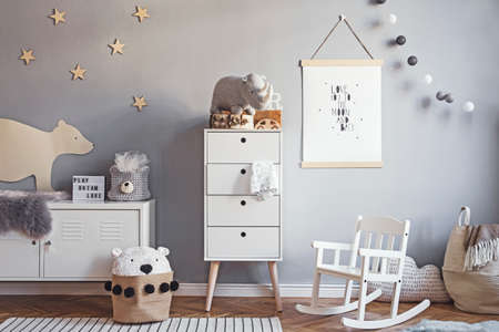 Scandinavian nursery room with mock up poster frame on the grey wall, white furniture, natural teddy bear and toys. Cute modern interior of playroom with white walls, baby accessories and toys.の写真素材