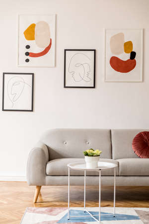 Stylish vintage decor in a spacious flat interior with design grey sofa, coffee table and posters on...