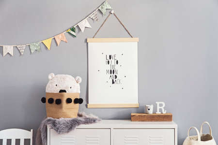Stylish and cute scandinavian decor of kid room with mock up poster, white shelf, natural toys, hanging decor flags , child's armchair, basket for accessories and teddy bears. Minimalistic concept.の写真素材