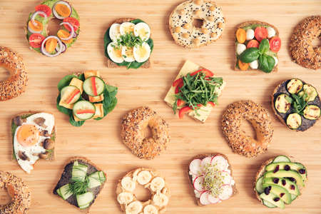 Stylish and tasty composition of vegan and vegetarian sandwiches with vegetables, herbs, paste, hummus and lettuce on the brown wooden table. Dark bread and bagels with seeds for breakfast.の写真素材