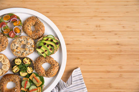 Stylish and tasty composition of vegan bagels sandwiches on the salver with vegetables, herbs, paste, seeds, hummus and lettuce on the brown wooden table. Fresh and healthy breakfast. Copy space.の写真素材