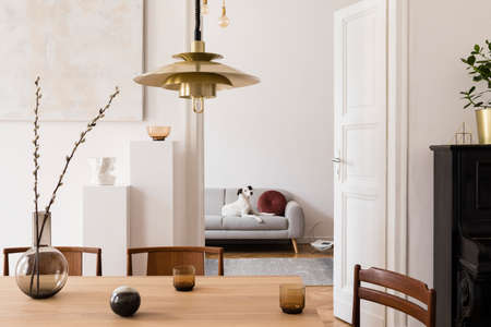 Stylish scandi interior of home space with design wooden table, chairs, sofa and gold pendant lamp....