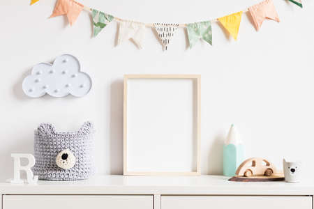 Stylish scandinavian newborn baby room with toys, teddy bear, accessories, ,cloud,colorful cotton flags and natural basket. Modern interior with mock up photo or poster frame. Real photo. Template.の写真素材