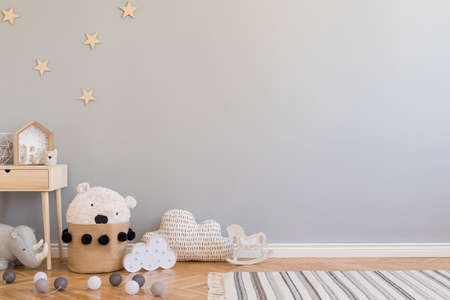 Stylish scandinavian newborn baby room with toys, children's chair, natural basket with teddy bear and small shelf. Modern interior with grey background walls, wooden parquet and stars pattern.の写真素材
