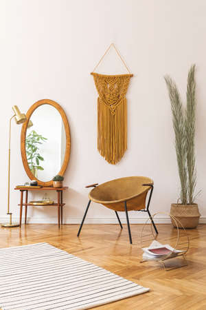 Stylish and minimalistic scandi interior of living room with design gold armchair, lamp, poster frames. dressing table with mirror, plants, palm leaves, yellow macrame and accessories. Cozy home decorの写真素材