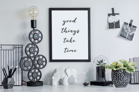 Stylish black and white home decor mock up. Creative desk with blank picture frame or poster, desk objects, office supplies, photos, elephant figure and plants in design pots on a white background.の写真素材