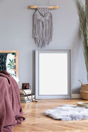 Stylish and luxury interior of bedroom with gray mock up frame, macrame and elegant accessories. Beautiful floral bed sheets, blankets and pillows. Modern home decor. Brown wooden parquet. Real photo.の写真素材