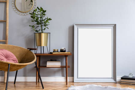 Stylish and luxury interior with design honey yellow armchair, gray mock up frame, gold mirror,...