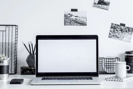 Stylish black and white home decor with mock up laptop screen. Creative desk with photos, desk objects, office supplies, cup of coffee on a white background. Open workspace for freelancer.の写真素材