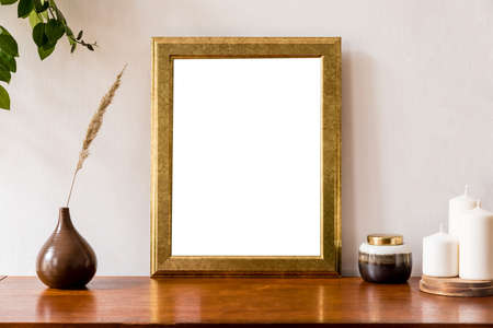Minimalistic and retro space of home interior with gold mock up poster frame, vintage cupboard with elegant accessories, flowers in vase, candles and box. Stylish home decor. White walls. Template.の写真素材