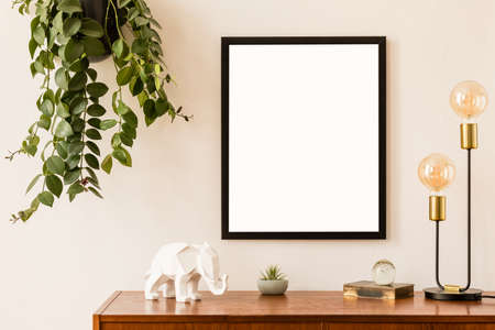 Minimalistic and stylish mock up poster frame concept with retro furnitures, hanging plant, gold table lamp and elegant accessories. White walls, home decor. Nice interior of living room. Real photo.の写真素材