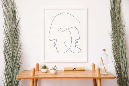 Stylish korean interior of living room with white mock up poster frame, elegant rattan accessories, wooden shelf and tropical palm leafs. Minimalistic concept of home decor. Template.の写真素材