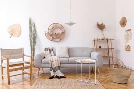 Stylish and cozy interior of living room with elegant rattan accessories, design armchair, gray sofa and wooden shelf. Korean style of home decor. Hanging rattan snail with airplants.の写真素材