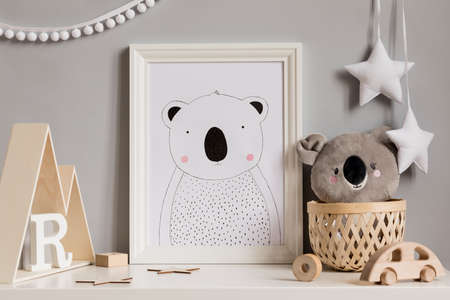 Stylish and cozy childroom with white mock up photo frame, wooden accessories and toys, koala bear,...