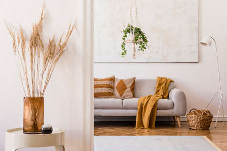 Minimalistic boho interior with design sofa, pillows, lamp, white coffee table with plant, flowers...
