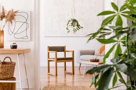 The nice boho open space interior at cozy apartment with design gray sofa, wooden desk, armchair, coffee table, plants, and elegant accessories. Mock up poster on the white wall. Stylish home decor.の写真素材