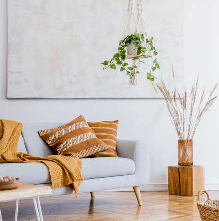 The modern boho compostion at living room interior with design gray sofa, wooden coffee table,...
