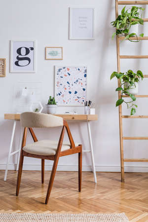 Design scandinavian interior of home office space with stylish chair, wooden desk, ladder, cube, elegant accessories and mock up posters frames. Stylish home decor. Template. White wall.の写真素材