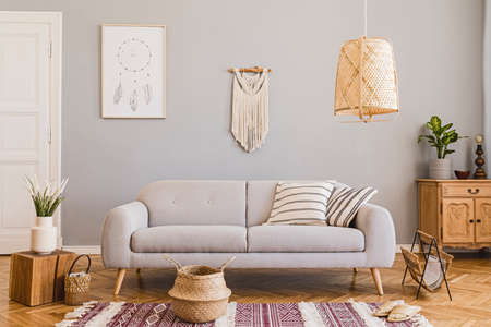 Stylish and design home interior of living room with gray sofa, wooden cube, commode, pillow, macrame, rattan lamp, basket, plants and elegant accessories. Stylish home decor. Template. Mock up poster.の写真素材