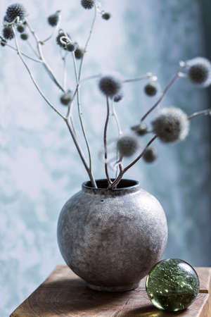 Stylish and chic composition of design vase with flowers and glassy ball on the wooden cube. Elegant accessories. Abstract paintings background wall. Template. Boho interior design at living room.の写真素材