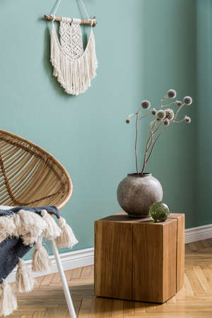 Interior design of living room at modern home with stylish rattan armchair, plaid, macrame, wooden...