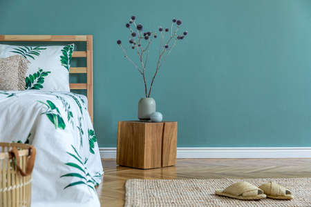 Minimalistic and boho interior design of bedroom with wooden cube, vase with flowers, rattan basket,...