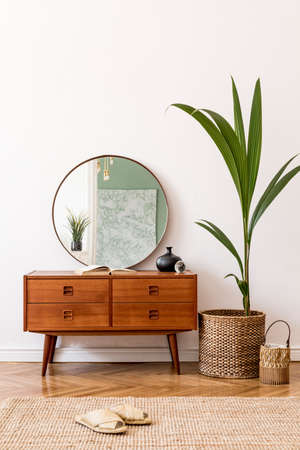Minimalistic and stylish composition of living room with wooden commode, mirror, tropicla plant in rattan basket and elegant personal accessories. Interior design, Home decor. template. White walls.の写真素材