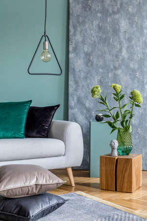 Stylish scandinavian interior design of living room with gray sofa, wooden cube, triangle lamp,...