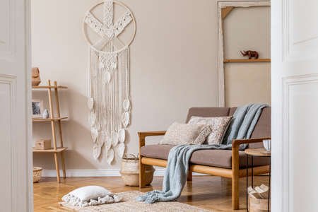 Interior design of living room with stylish brown wooden sofa, macrame, bookstand, lamp, coffee...