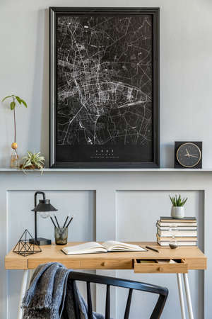 Stylish interior of home office room with black mock up poster map, wooden desk, black chair, clock,...