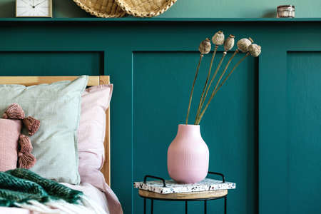 Modern bedroom interior with design coffee table, flowers in vase and elegant personal accessories. Beautiful bed sheets, blanket and pillows. Template. Stylish home staging. Wall panelling. Detailsの写真素材