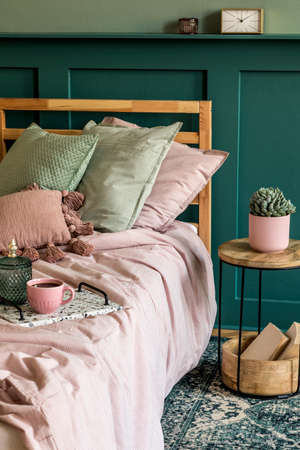 Stylish bedroom interior with design coffee table, plant, book, shelf and elegant personal accessories. Beautiful bed sheets, blanket and pillow. Template. Modern home staging. Wall panelling.の写真素材