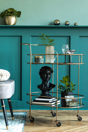 Stylish and modern composition of living room with design gold liquor cabinet, plants, books and...