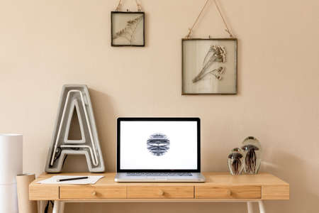Stylish and creative wooden desk with laptop mock up screen, photo frames, office accessories, plant...